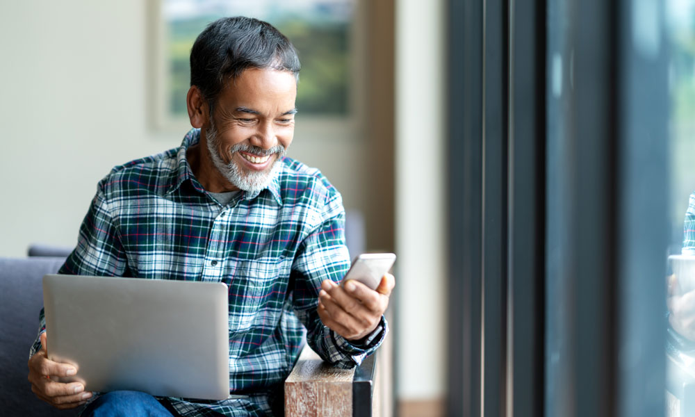 Instant Church Directory photo image showing an Asian man looking as his cell phone while holding a laptop computer