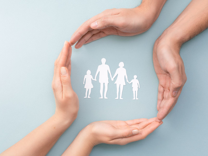 Photo of two sets of hands encompassing a paper silhouette of a family